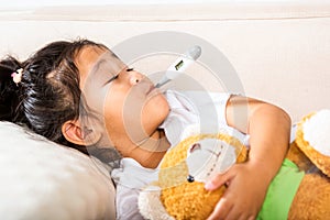 Mother checking temperature of her sick daughter with thermometer in mouth