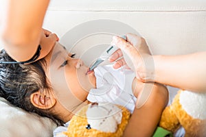 Mother checking temperature of her sick daughter with thermometer in mouth