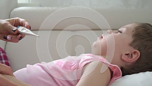 Mother checking temperature of her sick son. Sick child with fever and illness in bed