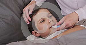 Mother checking temperature of unwell son in bedroom