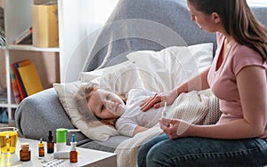 Mother checks daughter`s temperature on thermometer. There medicines on table