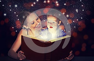 Mother and child baby daughter reading magic book in dark