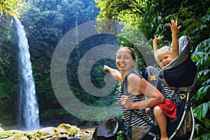 Mother with child in backpack hiking to jungle waterfall