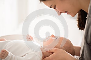 Mother and child on a bed. Mom and baby boy in diaper playing in sunny bedroom.