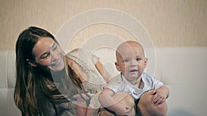 Mother and child on a bed. Mom and baby boy in diaper playing in sunny bedroom. Parent and little kid relaxing at home