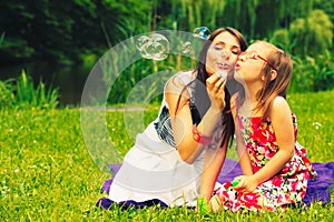 Mother and child blowing soap bubbles outdoor.