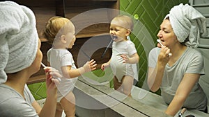 Mother and child brush teeth looking in mirror in bathroom