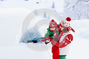 Mother and child brushing and shoveling snow off car after storm. Parent and kid with winter brush and scraper clearing family car