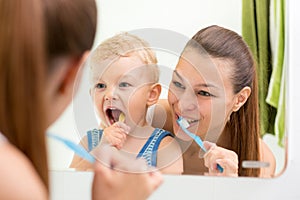 Mother and child brushing their teeth toothbrushes front of the mirror in the bathroom