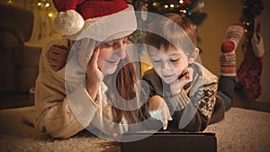 Mother with child on Christmas eve using digital tablet computer next to Christmas tree. Pure emotions of families and