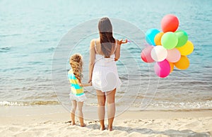 Mother and child with colorful balloons standing on beach near sea