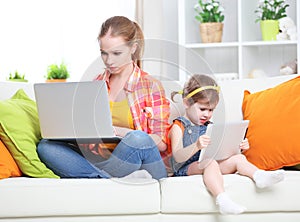 Mother and child with computer and tablet at home, according to