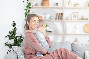 Mother-Child Connection. Happy Mom Hugging Her Toddler Baby While Relaxing On Couch