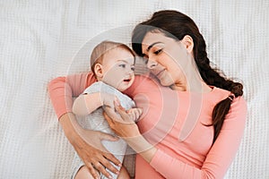 Mother and child connection. Young woman lying with her little child on bed, touching her baby& x27;s hand