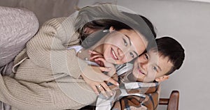 Mother and child in cozy casual clothes pose on a wooden chair. Studio shot.