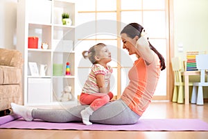 Mother and child daughter are engaged in fitness, yoga, exercise at home. Kid and woman swing press on stomach.