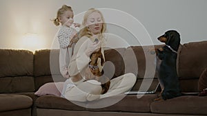 Mother and child daughter play with pets dog at home on sofa. Dachshund do trick, stand