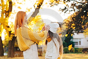 Mother and child daughter playing on autumn walk. Mom and girl laughing outdoors. Autumn fashion