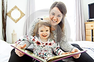 A mother and child daughter reading book in bed before going to sleep