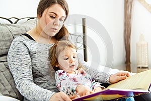 A mother and child daughter reading book in bed before going to sleep