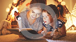 Mother and child daughter reading a book and a flashlight before