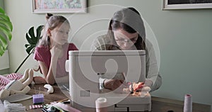 Mother and child daughter sewing together at home using sewing machine