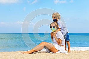 Mother, child in face masks have fun on sea beach