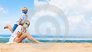 Mother, child in face masks have fun on sea beach