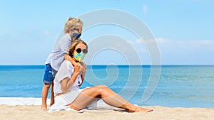 Mother, child in face masks have fun on sea beach