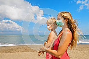 Mother, child in face masks on tropical sea beach