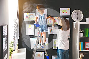 Mother and child girl hang their drawings on wall