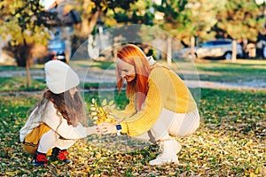 Mother and child girl playing with autumn leaves. Happy family enjoying autumn day together