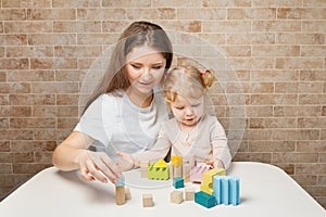 Mother and child girl playing with block toys on white table