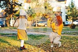 Mother and child girl throwing leaves in autumn park. Happy family enjoying autumn day