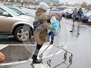 Mother and child go to the mall. Walking with an empty trolley in a parking lot