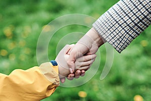 Mother and child hands holding each other on field. Support, help and trust. Kid and mother hands on nature background