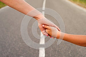 Mother and child hold hands together while walking along the highway in summer outdoors