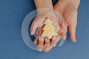 mother and child holding a Christmas tree cookie in hands, blue paper background