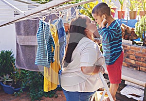 Mother, child and love for hanging washing with kiss or funny face with laundry housework, backyard or chore. Woman, son photo