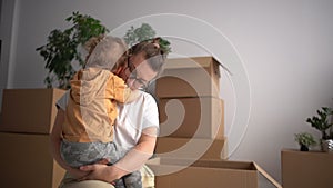 Mother and child, mom with toddler in her arms against the background of cardboard boxes, relocation and moving to a new