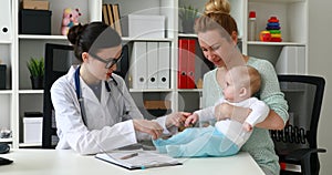 Mother with child at pediatrician reception in white room, checking motility skills of child.