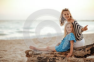Mother and child pointing at something while sitting on beach