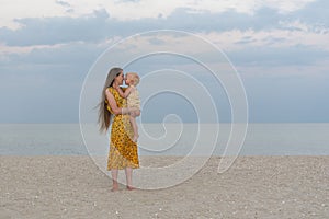 Mother and child on sandy beach on sea and sky background. Maternal care and love. Seaside holiday with baby