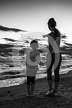 Mother and child on seashore on sunset pointing at something