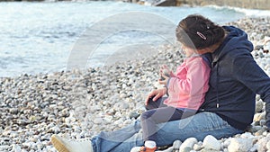 Mother and child sit on the beach and enjoy the sunset