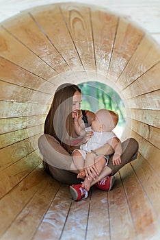 Mother and child are sitting inside the wooden tunnel on Playground. Vertical frame