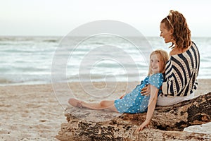 Mother and child sitting on wooden log on beach in evening