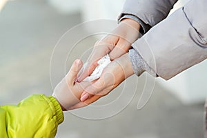Mother and child on the street disinfecting hands with a wet wipe, close up. Woman cleaning kid hands with antiseptic tissue