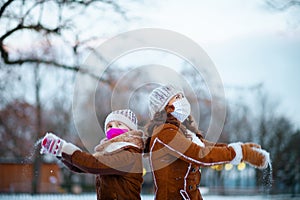 Mother and child throwing snow outside in city park in winter