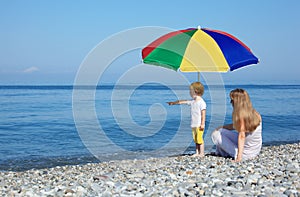 Mother with child under umbrella on pebble beach